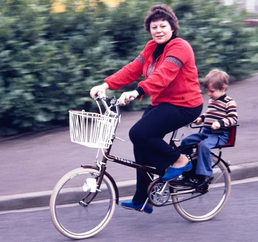 Restored slide of a woman cycling with a young child seated behind her